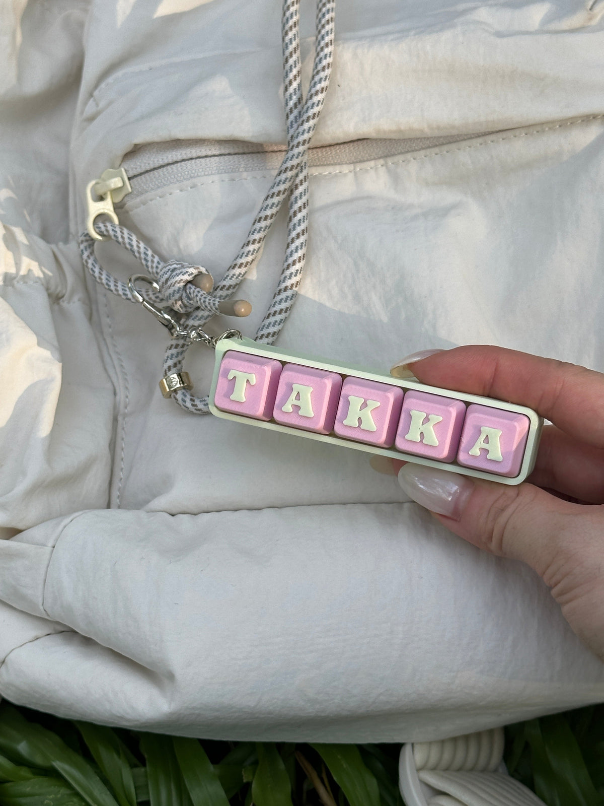 Personalized TAKKA keyboard key toy held against a white backpack
