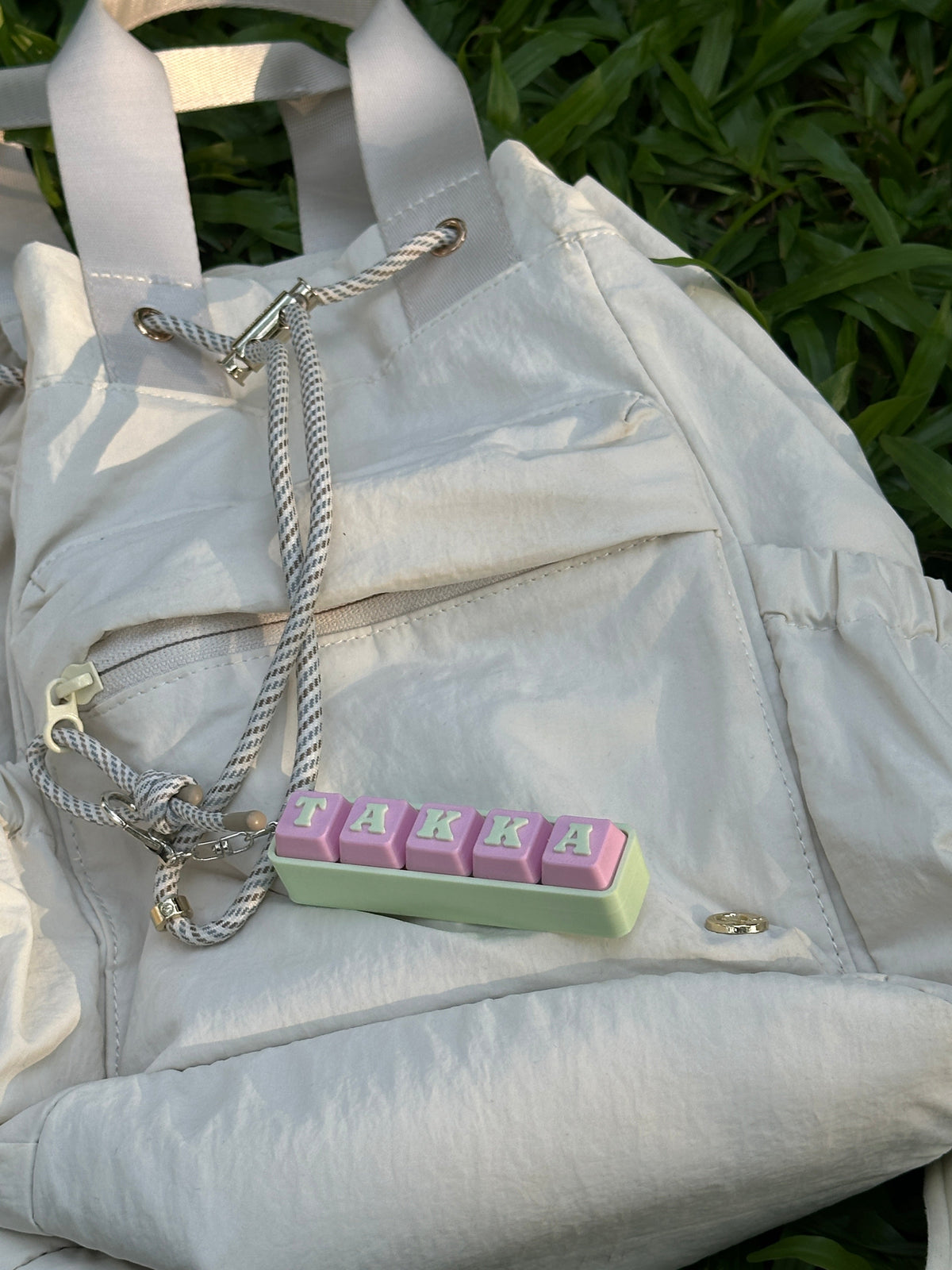 Personalized TAKKA keyboard key toy displayed on a white backpack outdoors